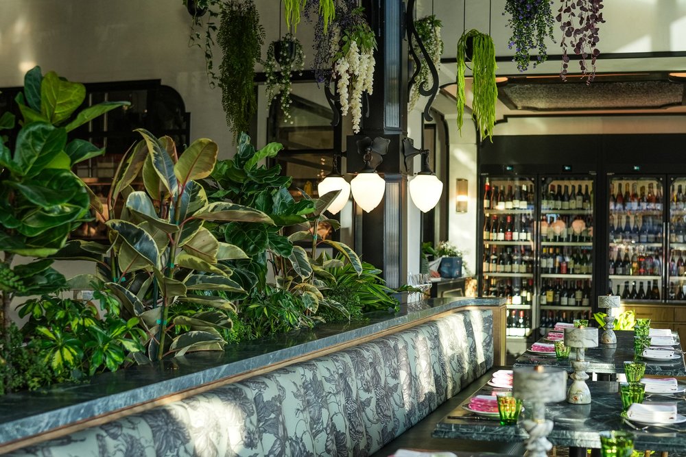 Leafy greenery above a floral banquette and set tables at À L’ouest in North Park.