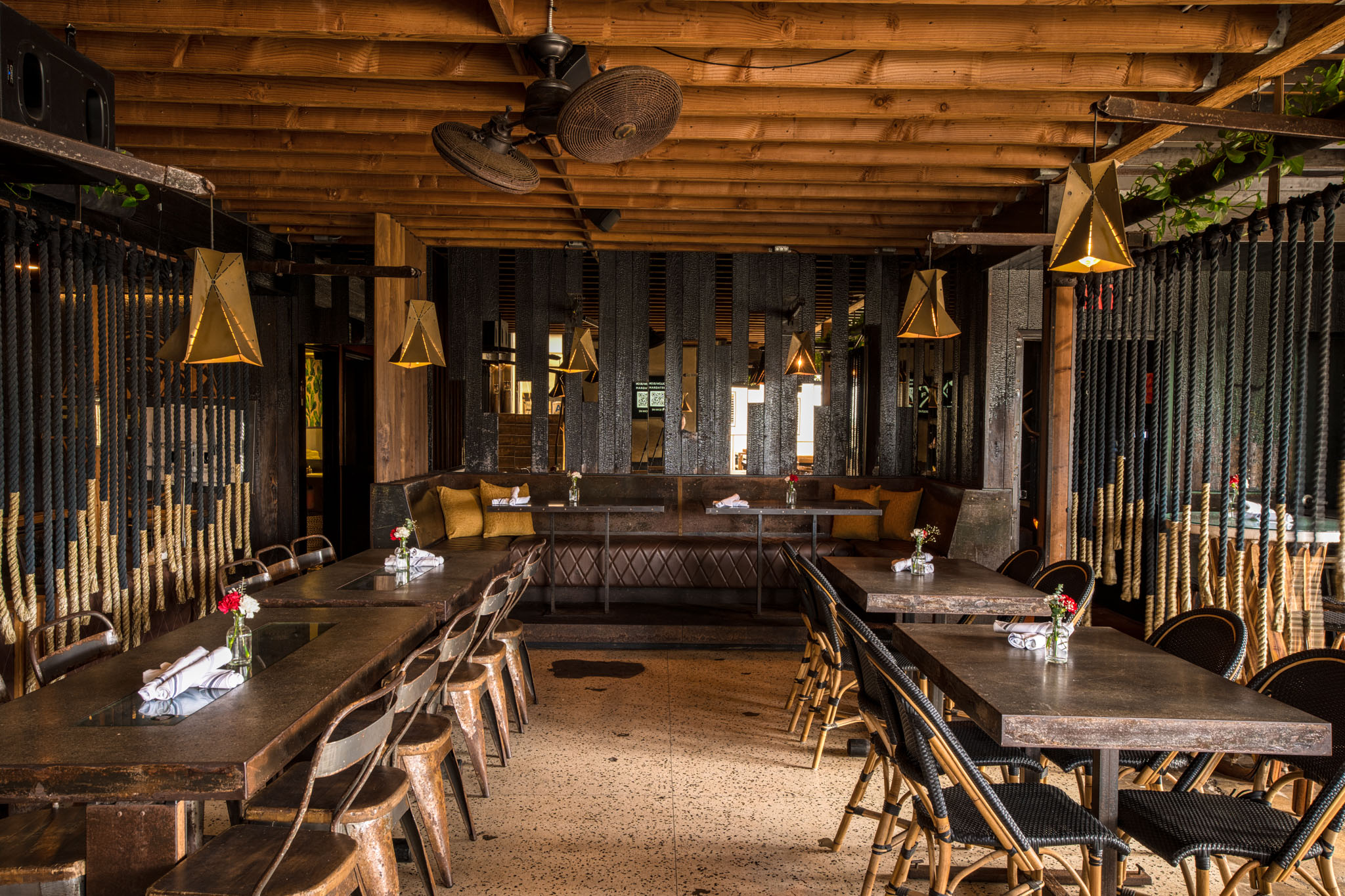 Firehouse dining area with wooden beams, hanging lights, rope dividers and leather banquette