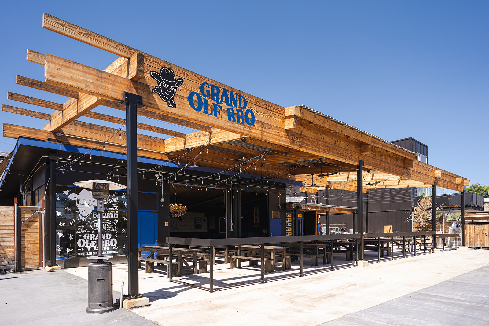 Grand Ole BBQ y Asado North Park patio with picnic tables beneath a large wooden pergola and sign
